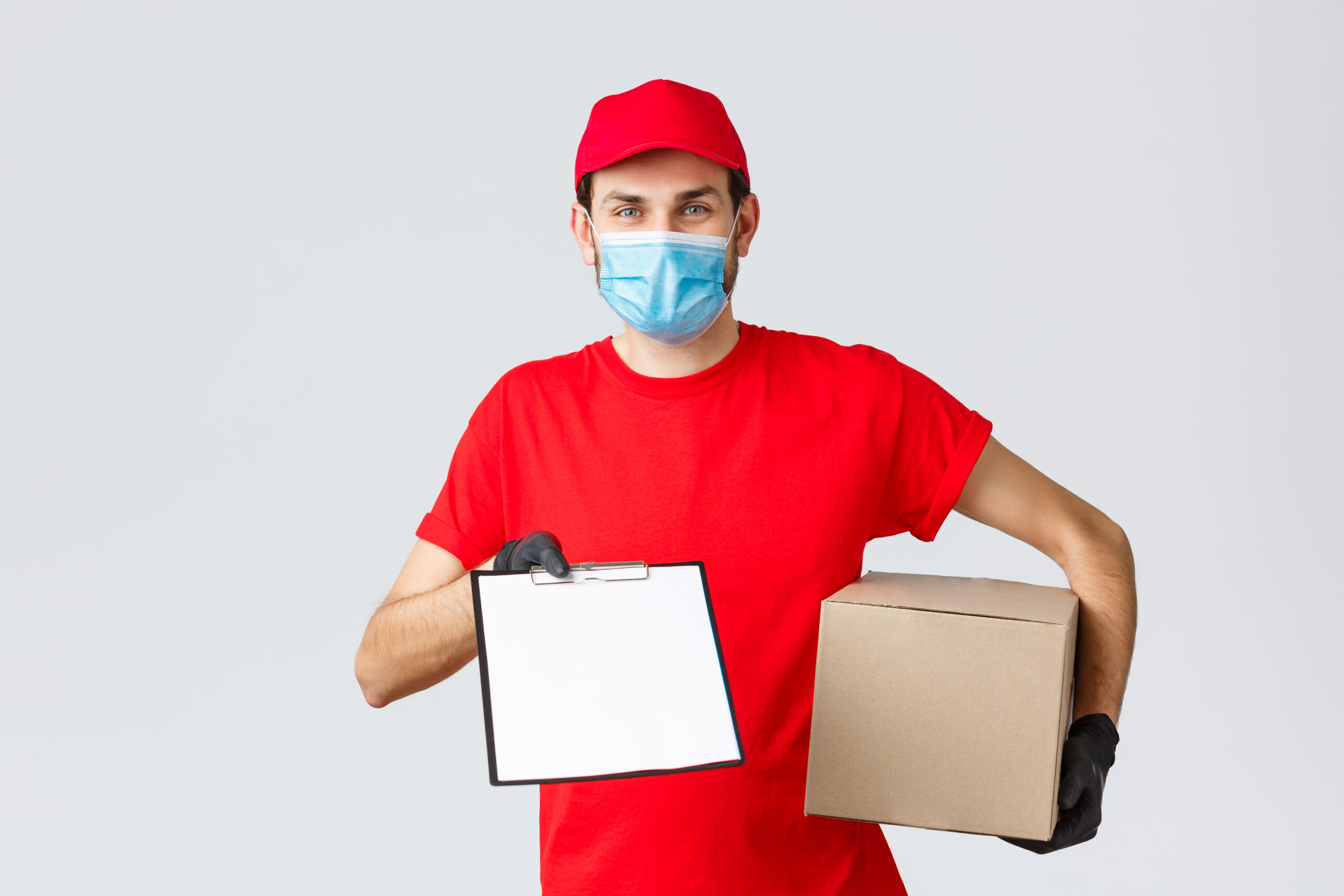Packages and parcels delivery, covid-19 quarantine delivery, transfer orders. Friendly courier in red uniform, face mask and gloves, holding package box and give clipboard order sign form to client.